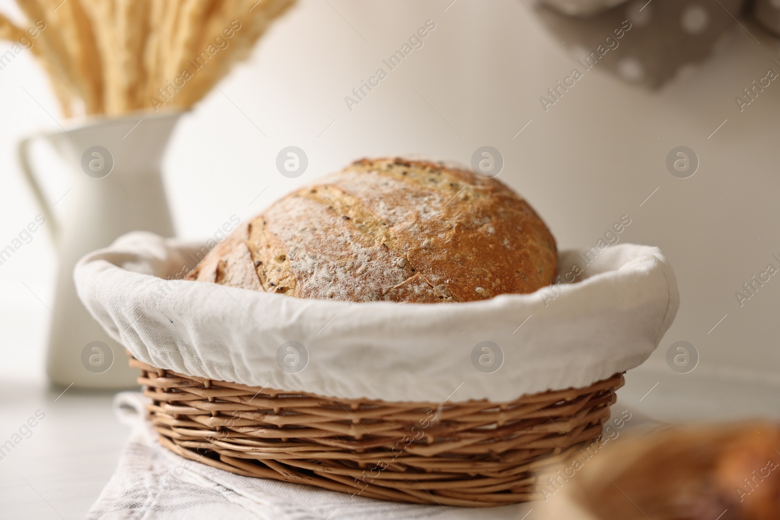 Photo of Wicker bread basket with freshly baked loaf on white marble table in kitchen, closeup