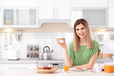 Photo of Beautiful woman eating tasty toasted bread with jam in kitchen