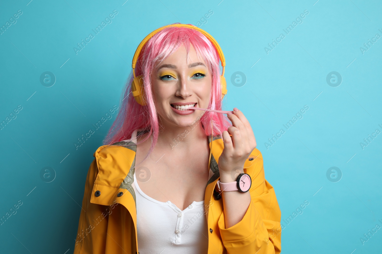 Photo of Fashionable young woman in pink wig with headphones chewing bubblegum on yellow background