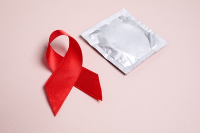 Photo of Red ribbon and condom on pink background, closeup. AIDS disease awareness