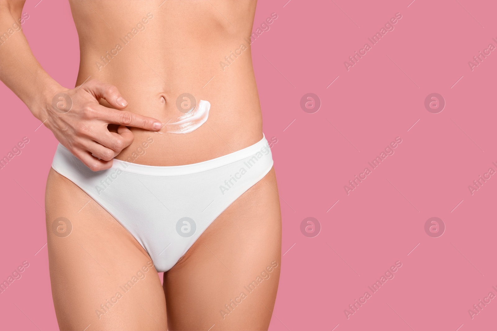 Photo of Woman applying body cream onto her belly against pink background, closeup. Space for text