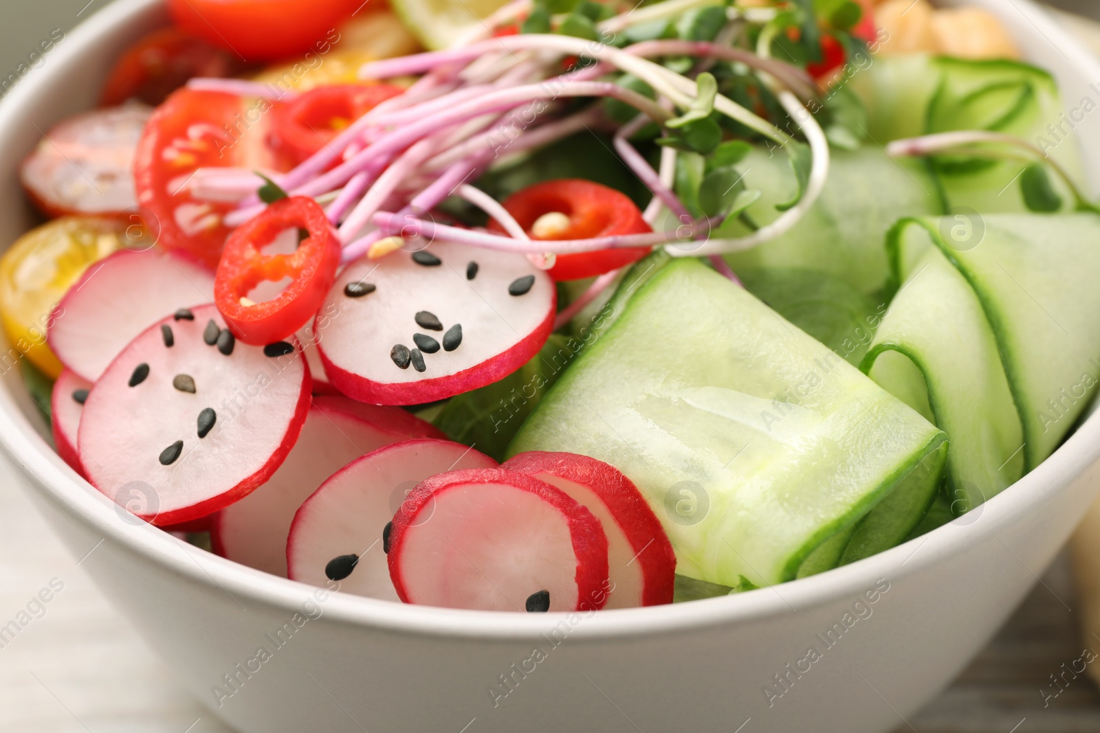 Photo of Bowl with many different vegetables on white wooden table, closeup. Vegan diet