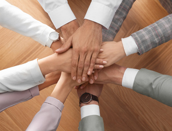 Photo of People holding hands together over wooden background, top view. Unity concept