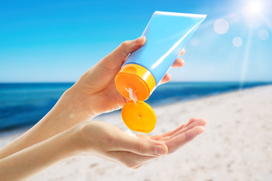 Young woman applying sun protection cream near sea, closeup