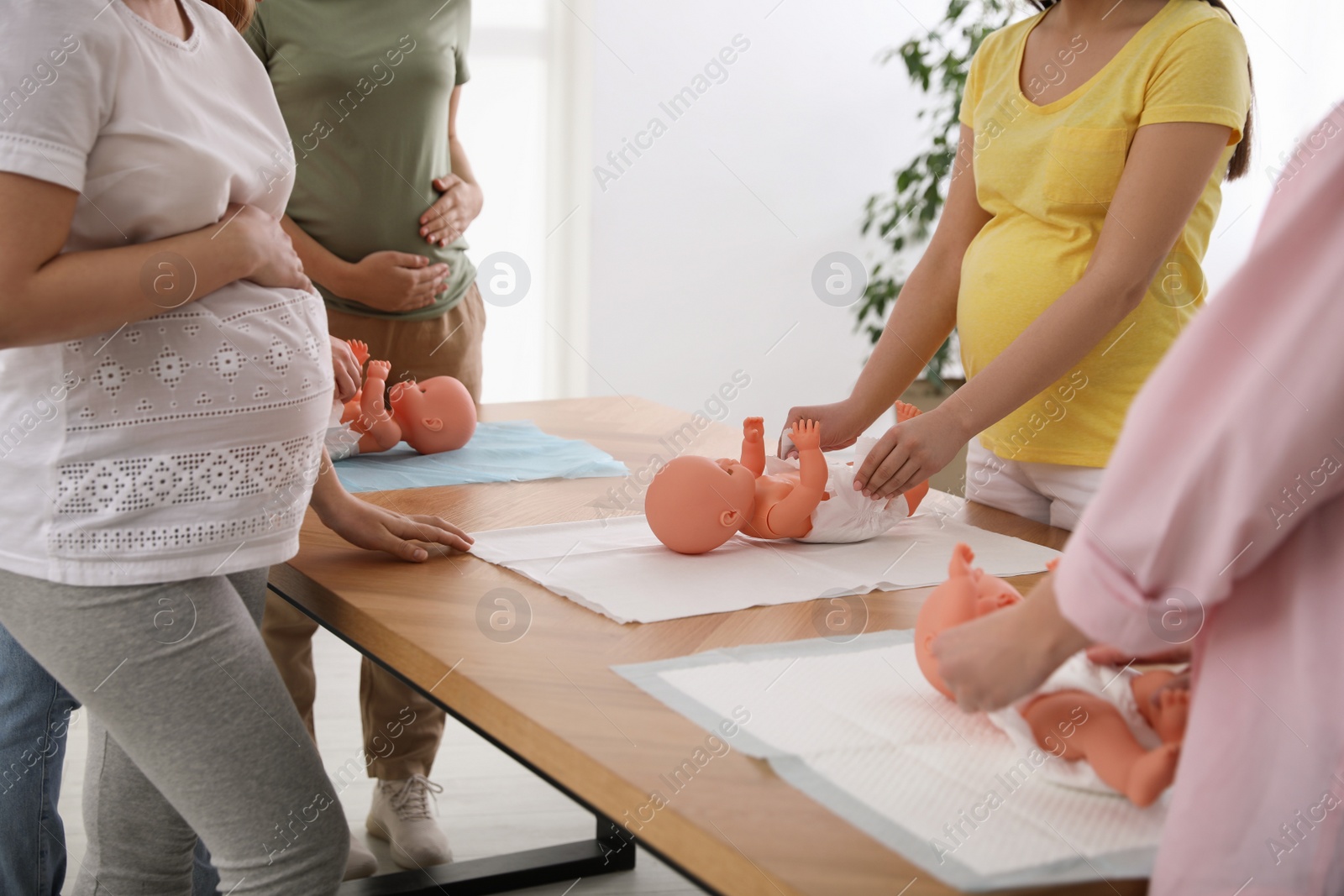 Photo of Pregnant women learning how to swaddle baby at courses for expectant mothers indoors, closeup