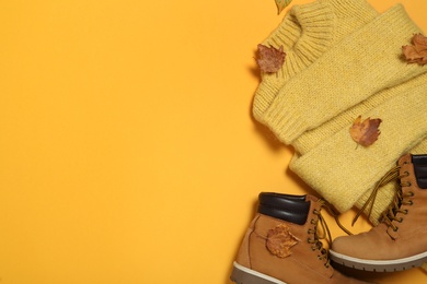 Photo of Boots, dry leaves and sweater on yellow background, flat lay with space for text. Autumn season