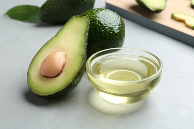 Photo of Bowl of natural oil and avocados on grey stone background