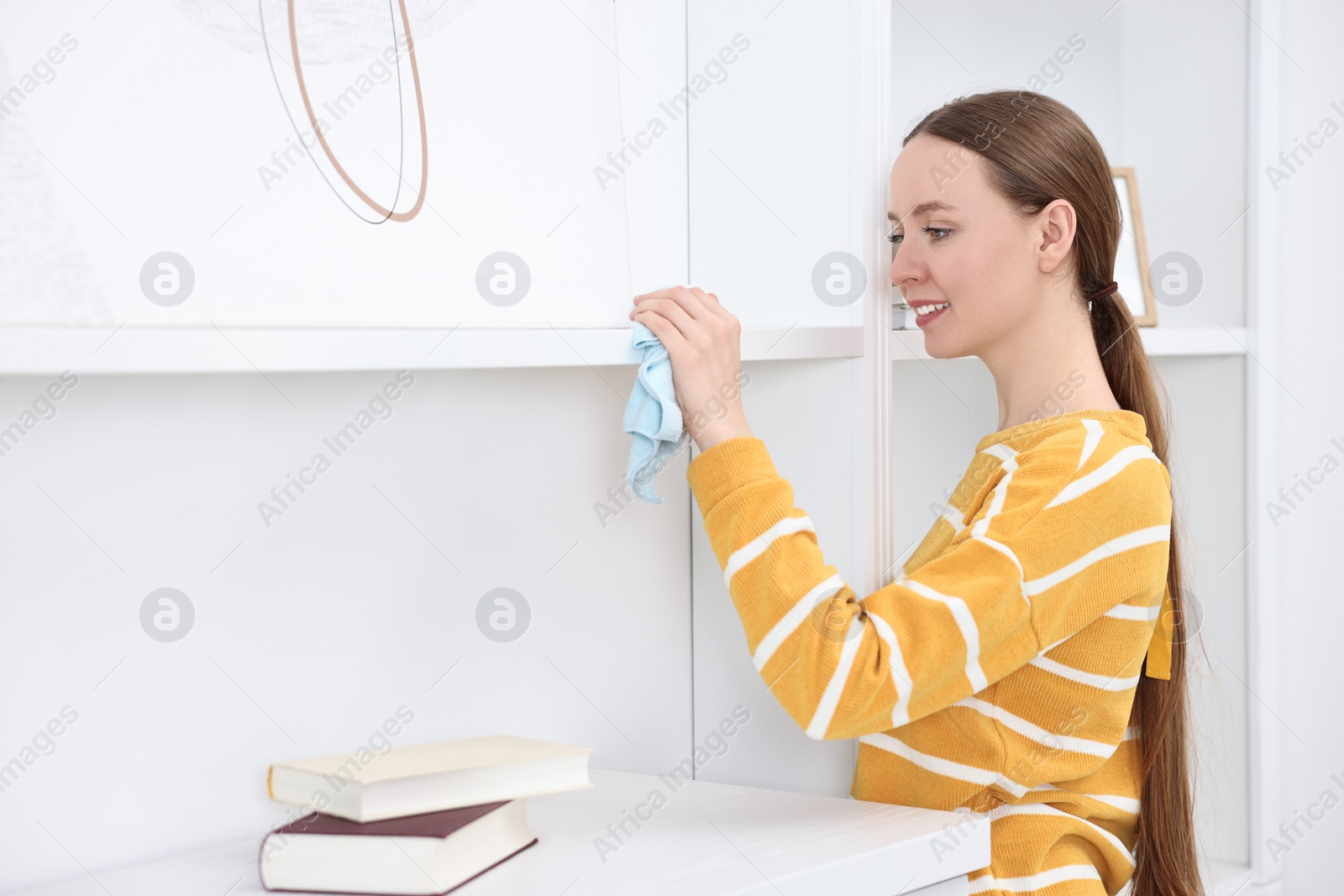 Photo of Woman cleaning shelf with rag at home