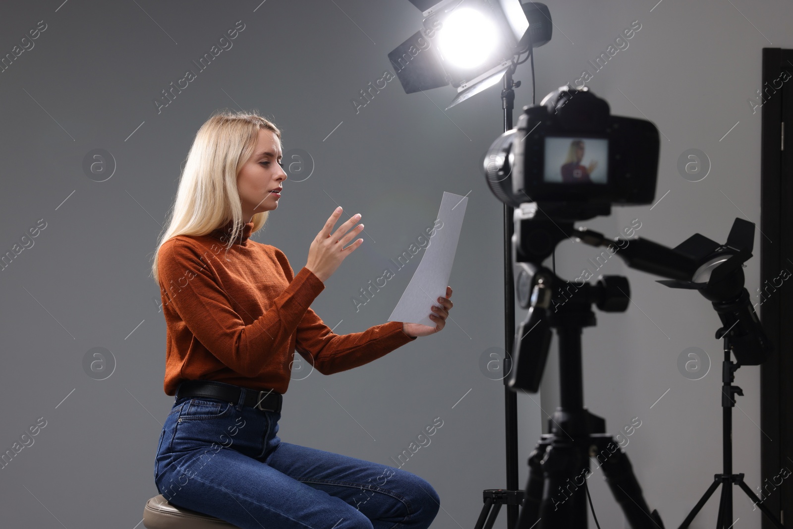 Photo of Casting call. Emotional woman with script sitting on chair and performing in front of camera in studio