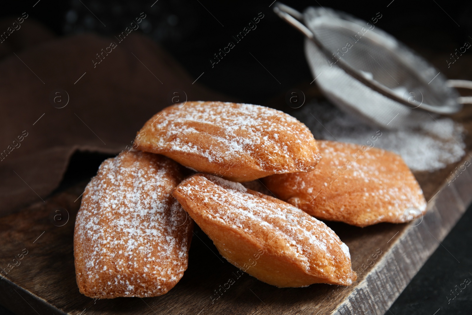 Photo of Delicious madeleine cakes with powdered sugar on wooden board, closeup