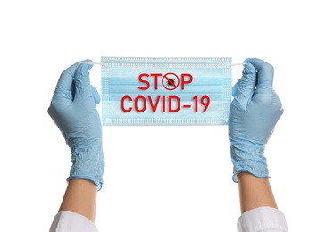 Doctor holding medical mask with text Stop Covid-19 on white background, closeup. Protective measures during pandemic