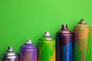 Photo of Used cans of spray paints on green background, flat lay with space for text. Graffiti supplies
