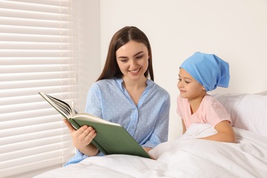 Childhood cancer. Mother and daughter reading book in hospital