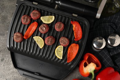 Photo of Electric grill with meat balls, bell peppers and lemon on grey table, flat lay