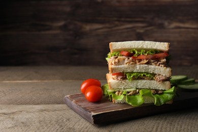 Delicious sandwich with tuna, tomatoes and lettuce on wooden table, space for text