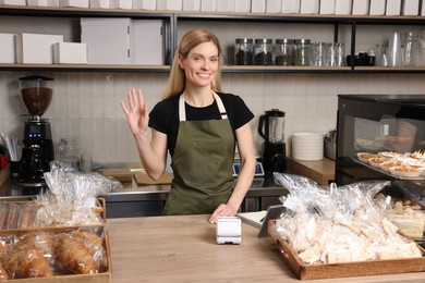 Photo of Happy seller at cashier desk in bakery shop