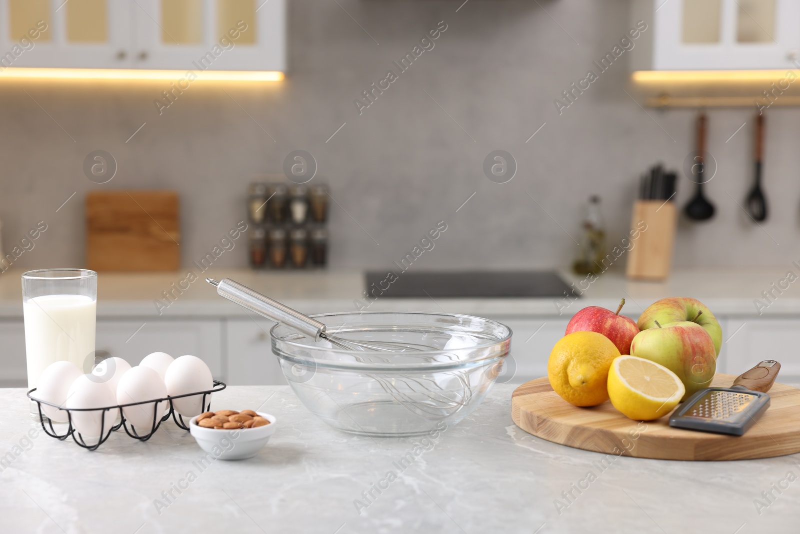 Photo of Metal whisk, bowl, grater and different products on gray marble table in kitchen