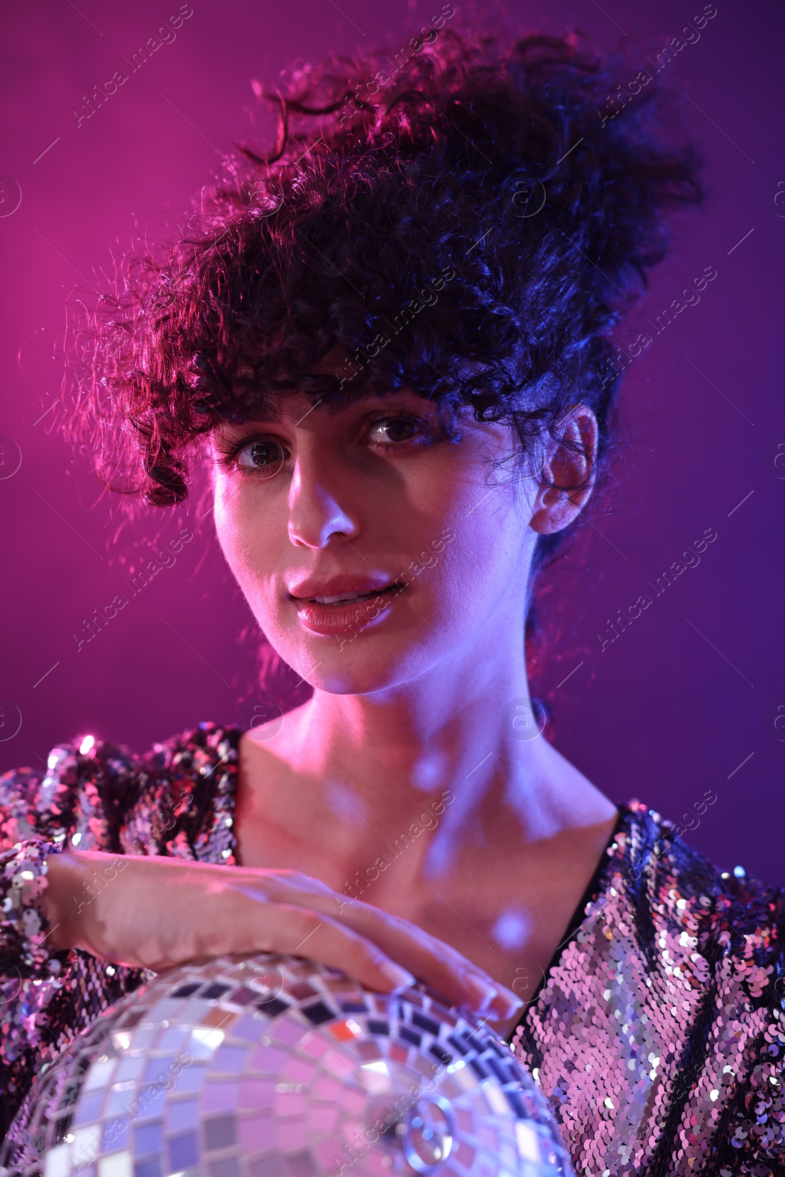 Photo of Beautiful young woman with disco ball posing on color background in neon lights