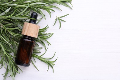 Fresh green rosemary and bottle of essential oil on white wooden table, flat lay. Space for text