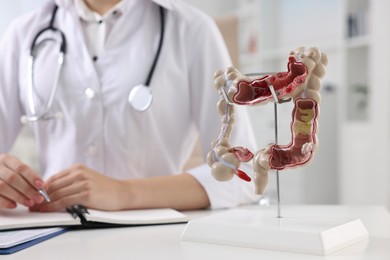 Photo of Gastroenterologist working at table in clinic, focus on anatomical model of large intestine