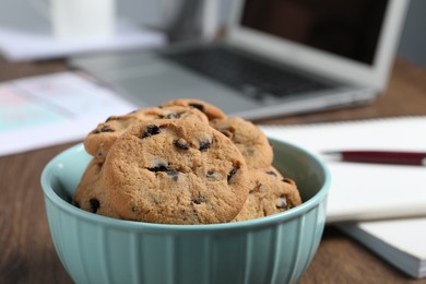 Bowl with chocolate chip cookies on table in office, closeup