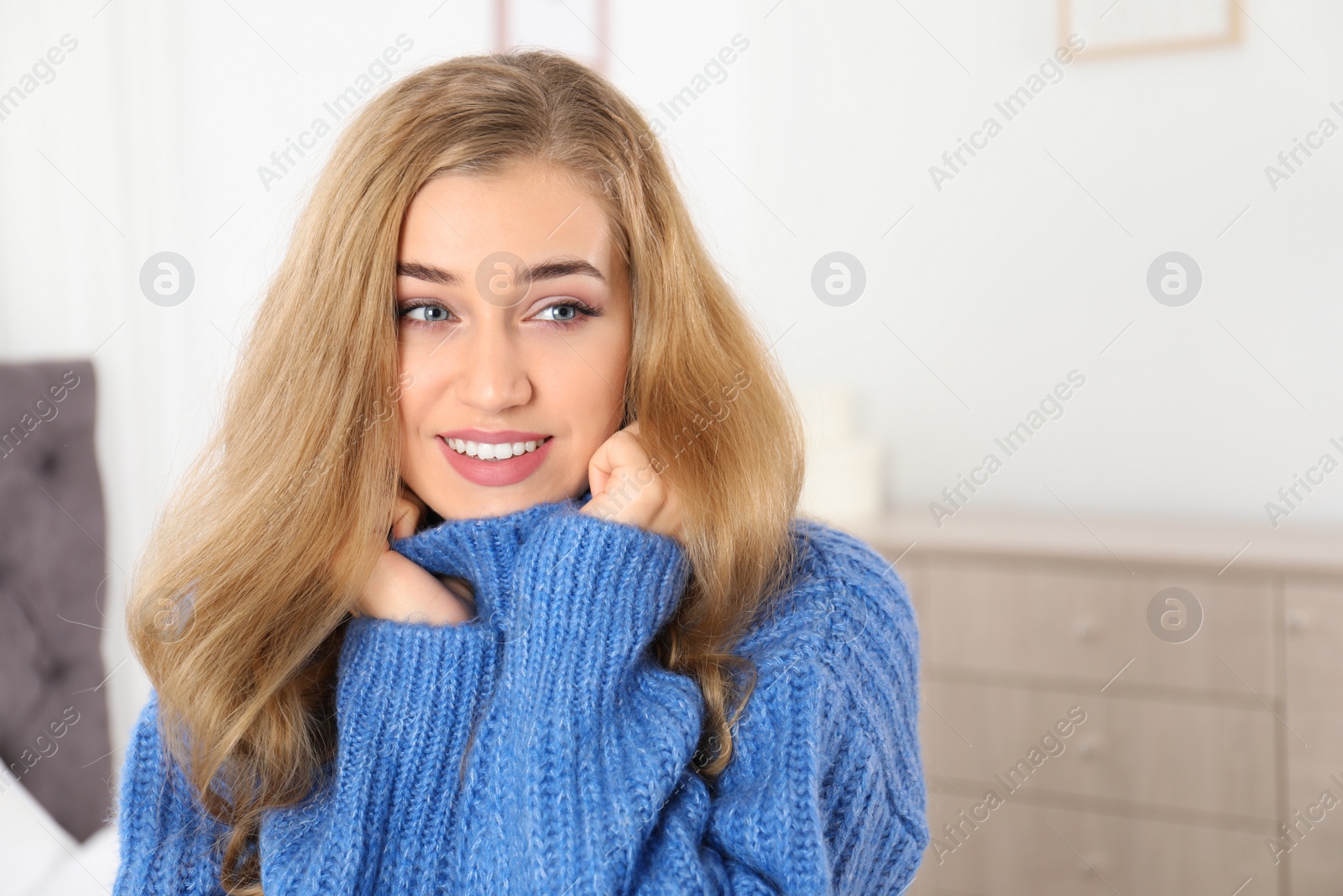 Photo of Beautiful smiling young woman in cozy warm sweater at home. Space for text