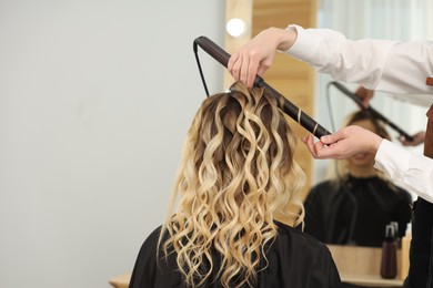 Photo of Hair styling. Hairdresser curling woman's hair in salon, closeup. Space for text