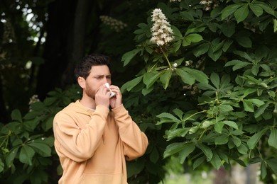 Man suffering from seasonal spring allergy near tree in park