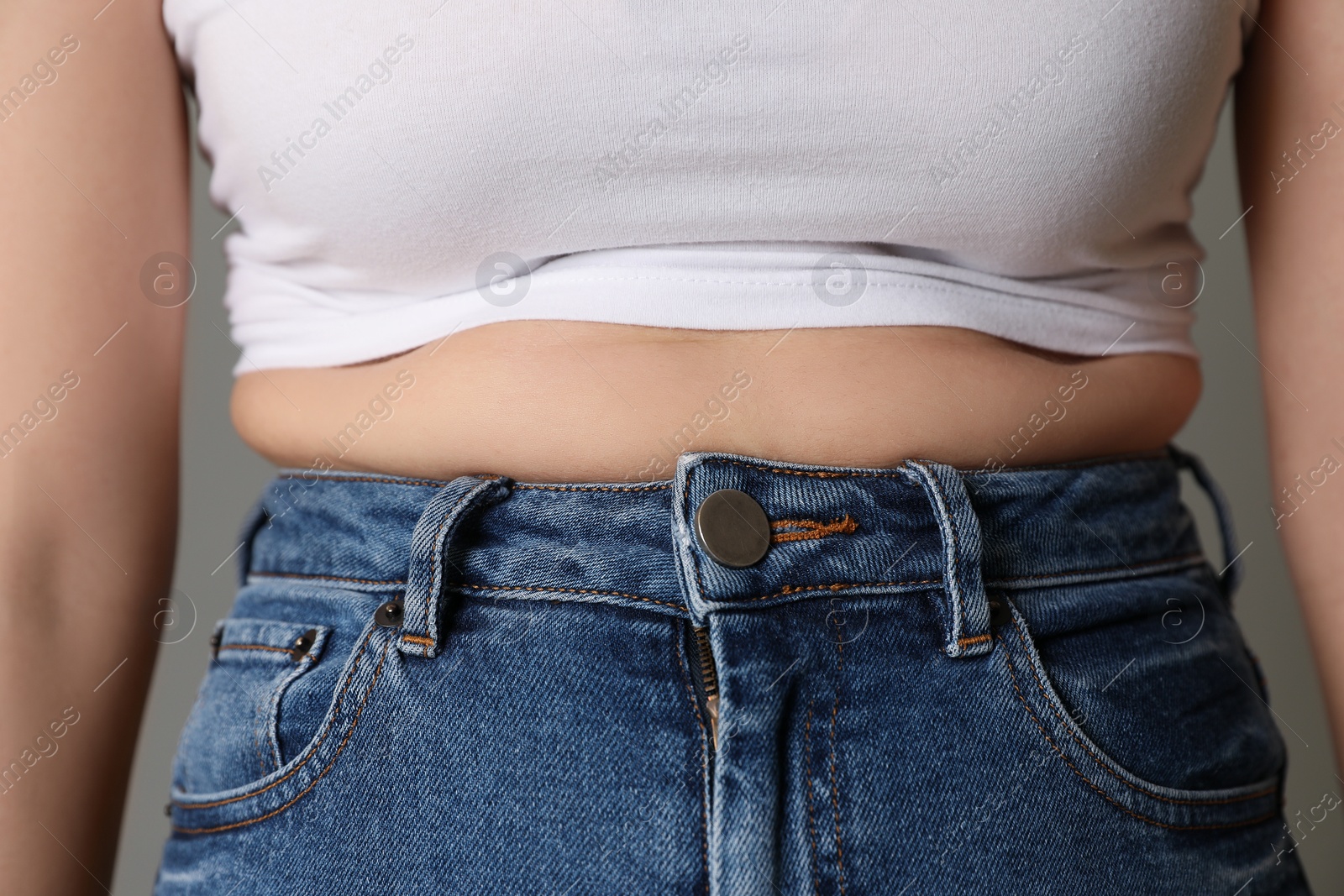 Photo of Overweight woman in tight tshirt and jeans on grey background, closeup