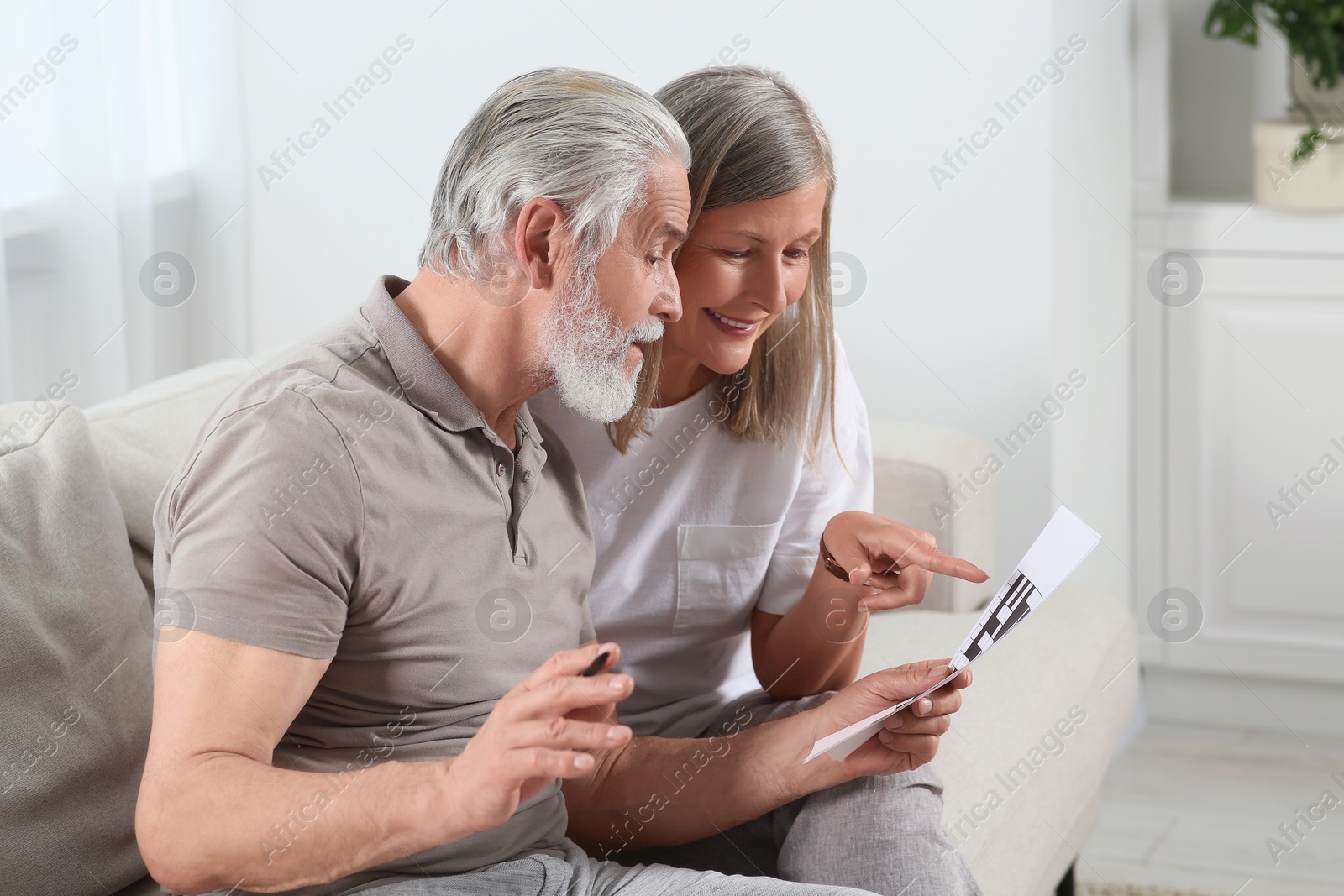Photo of Senior couple solving crossword on sofa at home