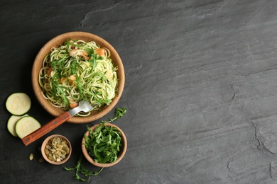 Photo of Delicious zucchini pasta with shrimps and arugula served on black slate table, flat lay. Space for text
