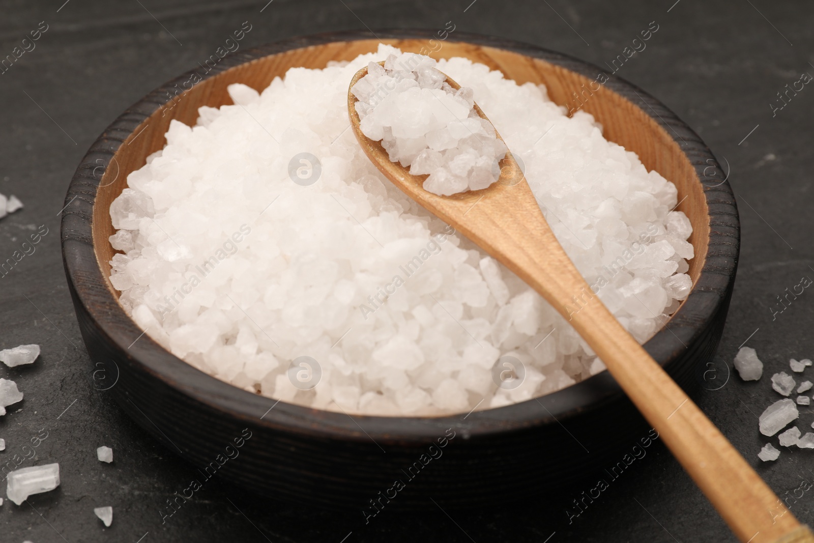 Photo of Bowl and spoon with sea salt on black table, closeup