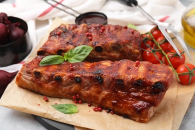 Photo of Tasty roasted pork ribs served with sauce, basil and tomatoes on grey table, closeup