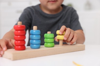 Photo of Motor skills development. Little boy playing with stacking and counting game at table indoors, closeup