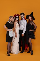Group of people in scary costumes on orange background. Halloween celebration