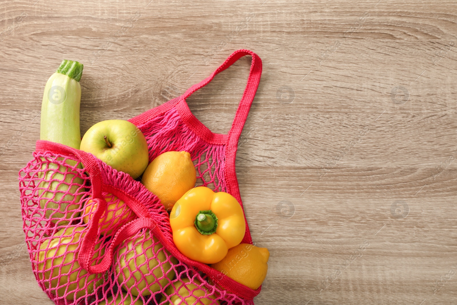 Photo of Net bag with vegetables and fruits on wooden table, top view. Space for text