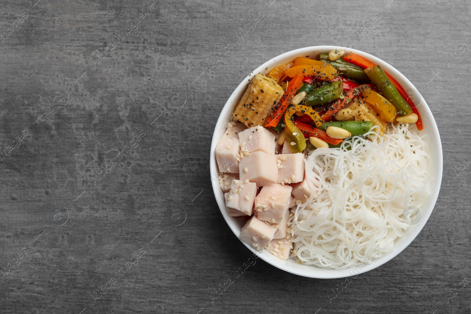 Photo of Tasty cooked rice noodles with chicken and vegetables on grey table, top view. Space for text