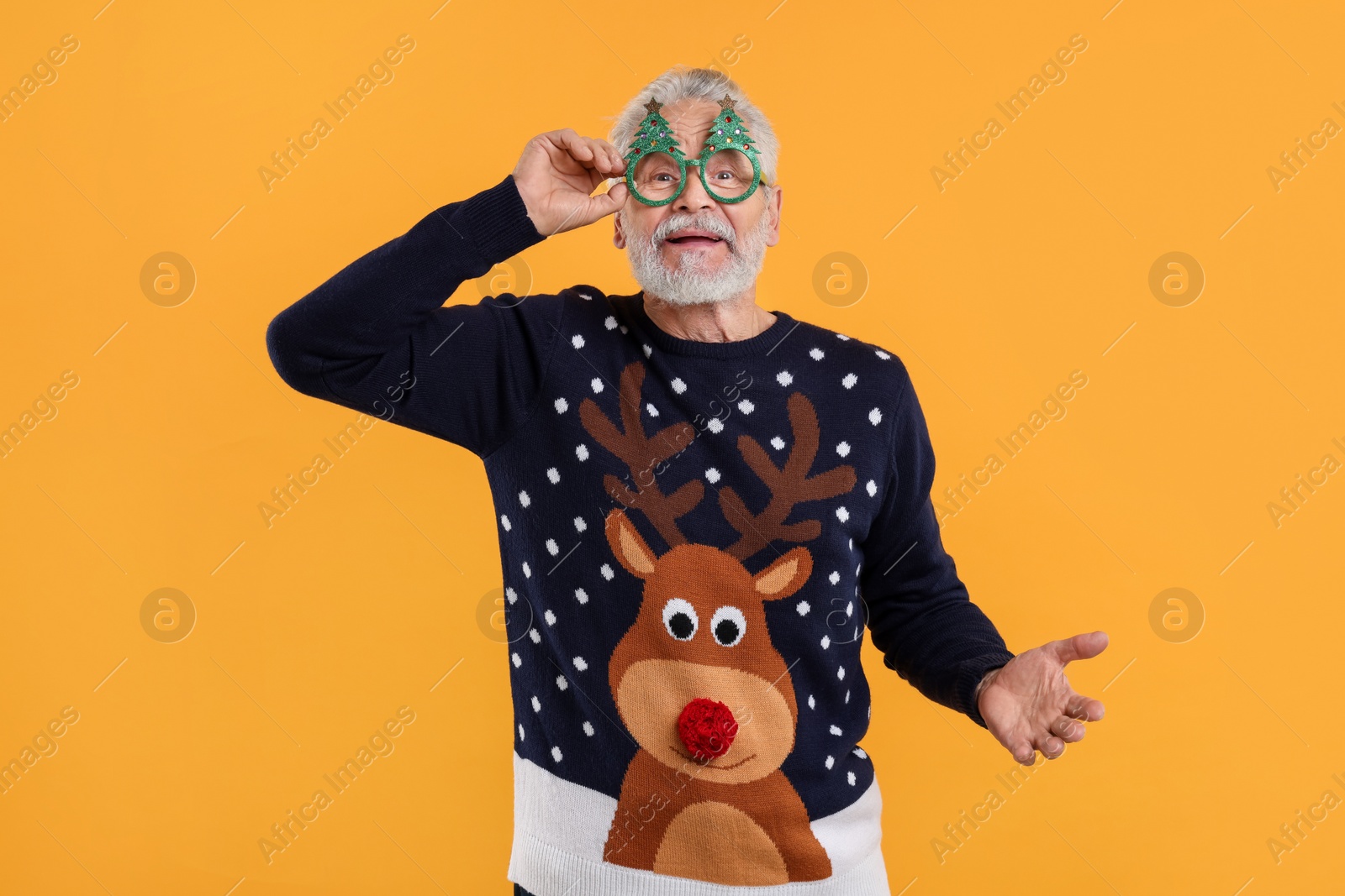 Photo of Senior man in Christmas sweater and funny glasses against orange background