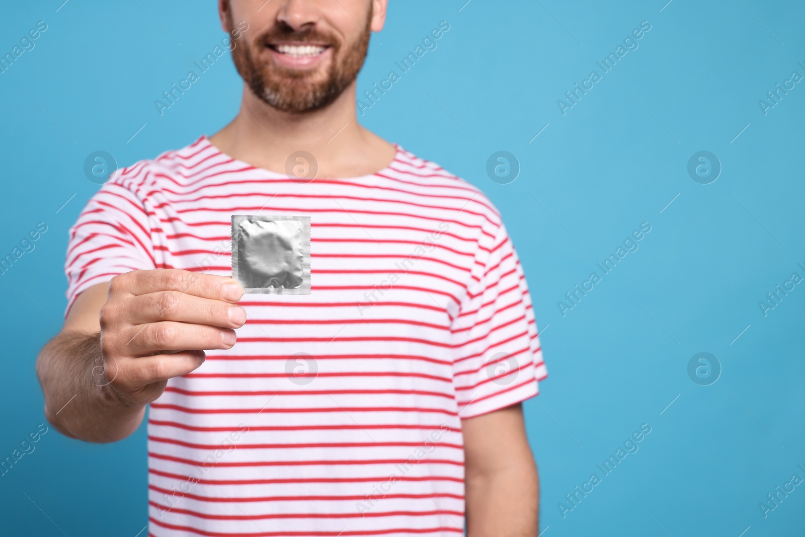 Photo of Closeup view of happy man with condom on light blue background, space for text. Safe sex