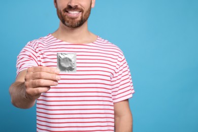 Photo of Closeup view of happy man with condom on light blue background, space for text. Safe sex