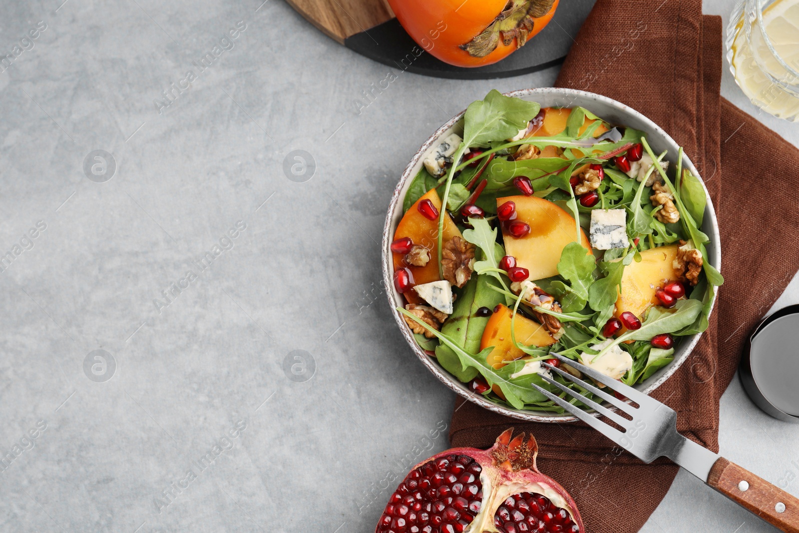 Photo of Tasty salad with persimmon, blue cheese, pomegranate and walnuts served on light grey table, flat lay. Space for text