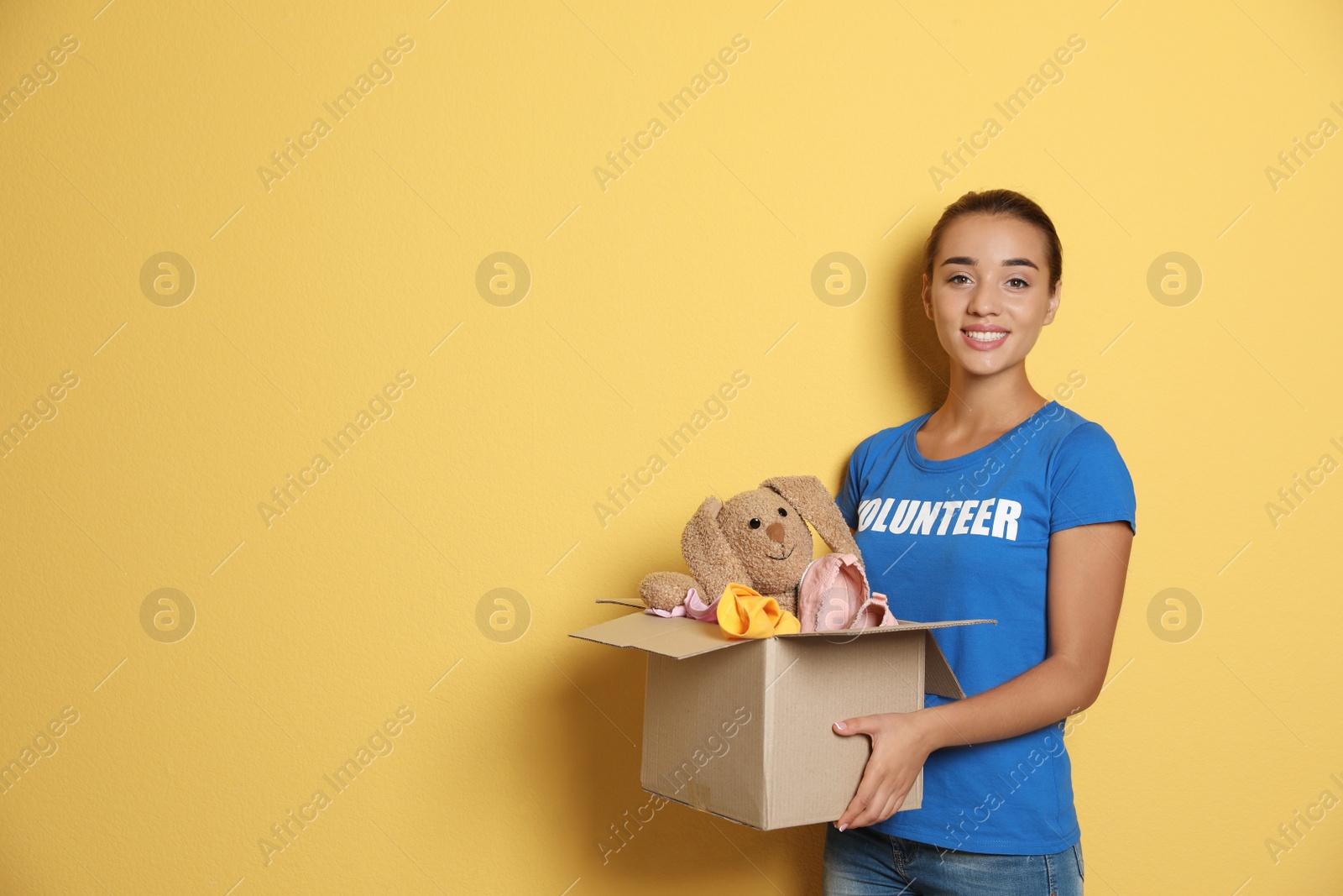 Photo of Female volunteer holding box with donations on color background. Space for text