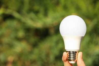Photo of Woman holding LED light bulb on blurred green background, closeup. Space for text