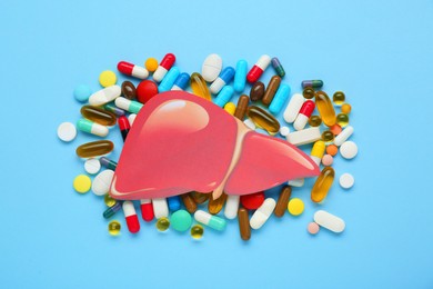 Photo of Paper liver and pills on light blue background, flat lay. Hepatitis treatment