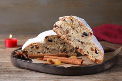Photo of Wooden plate of cut delicious Stollen sprinkled with powdered sugar and ingredients on table, closeup