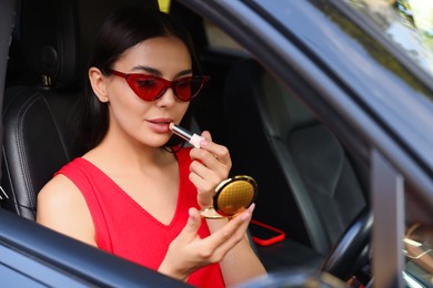 Photo of Beautiful woman with cosmetic pocket mirror applying lipstick in car