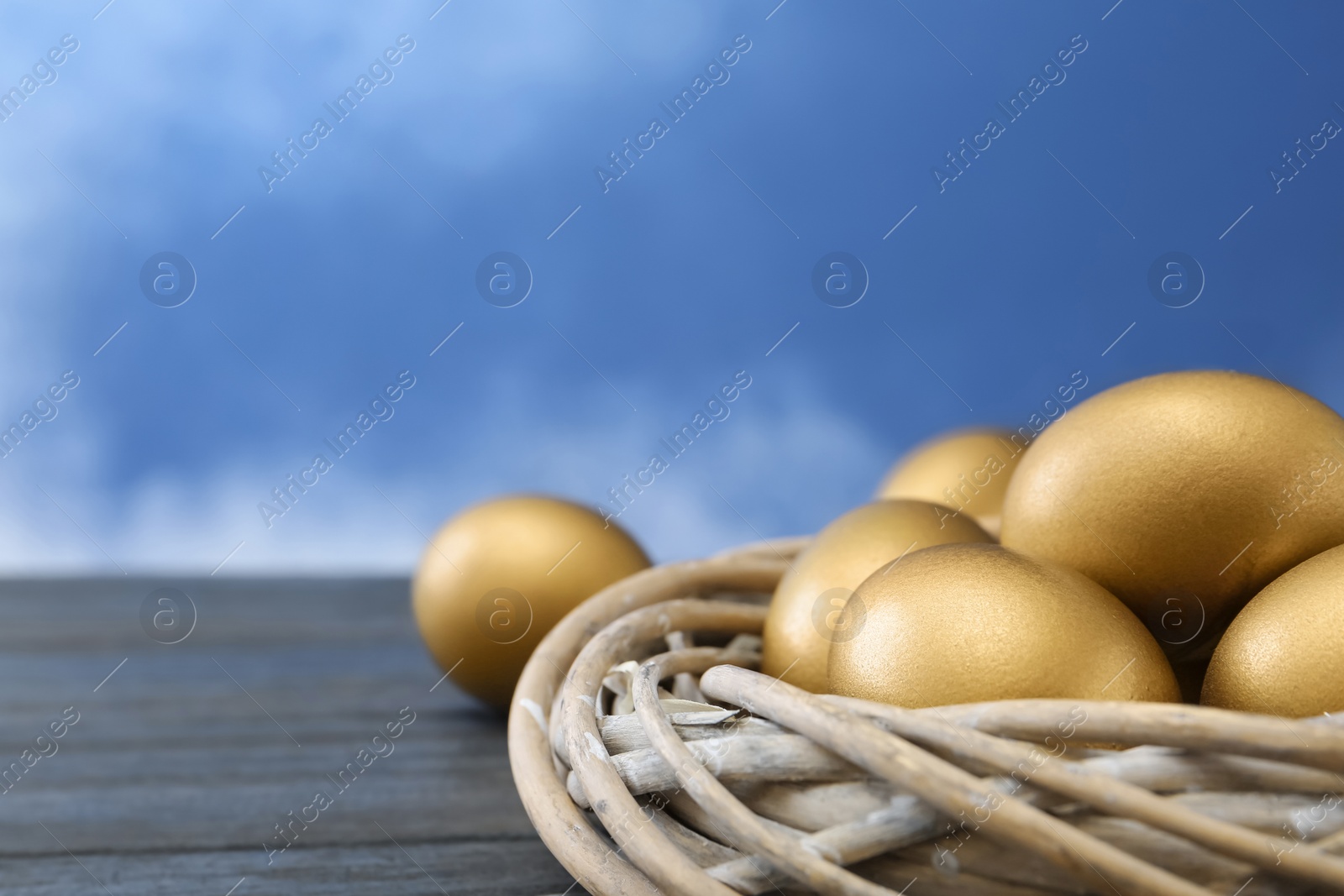 Photo of Golden eggs in nest on wooden table against color background, space for text