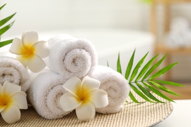 Photo of Spa composition. Towels, plumeria flowers and palm leaves on table indoors, closeup