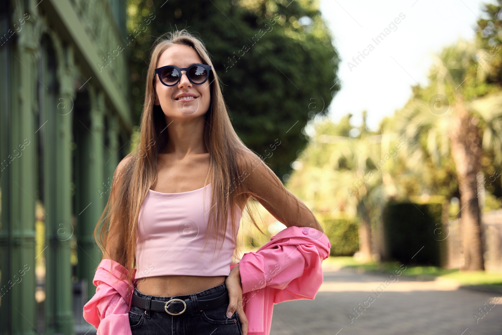 Photo of Beautiful young woman in stylish sunglasses on city street, space for text