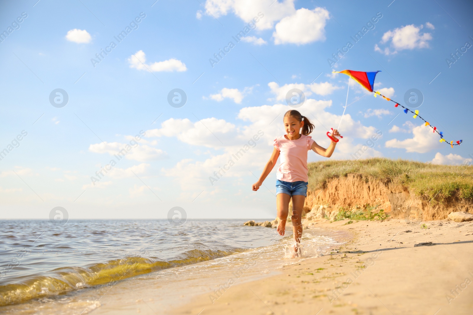 Photo of Cute little child with kite running on beach near sea. Spending time in nature